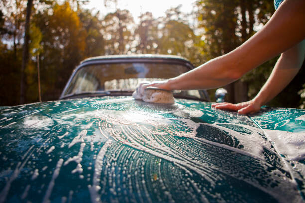 Young woman washing car at home in driveway.